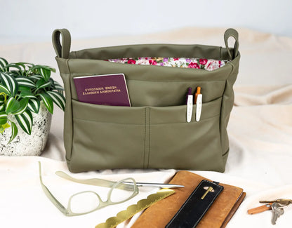 Green bag with compartments containing a passport, sunglasses, and other items on a light background.