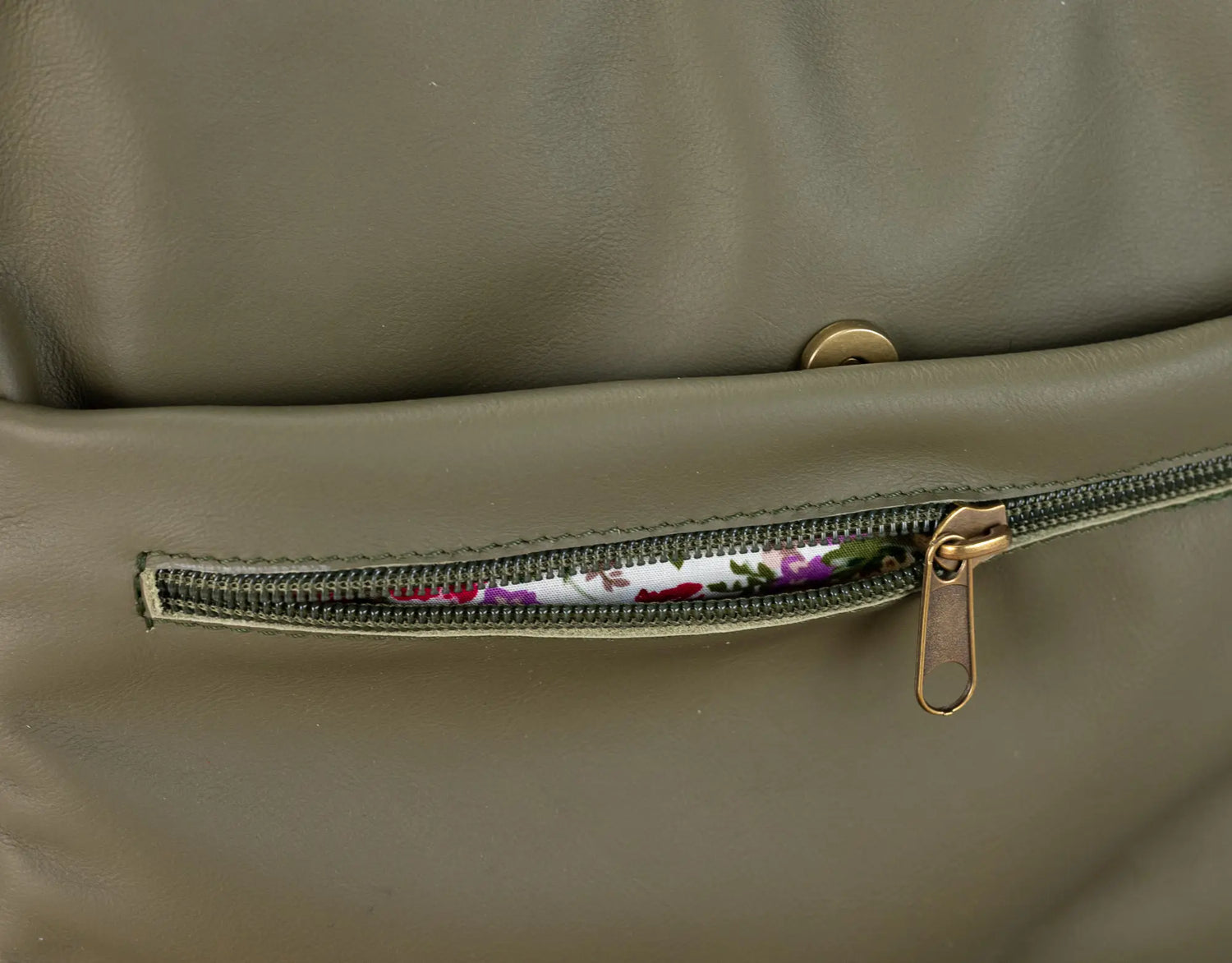 Close-up of a green leather bag with a zipper pocket showing floral lining.