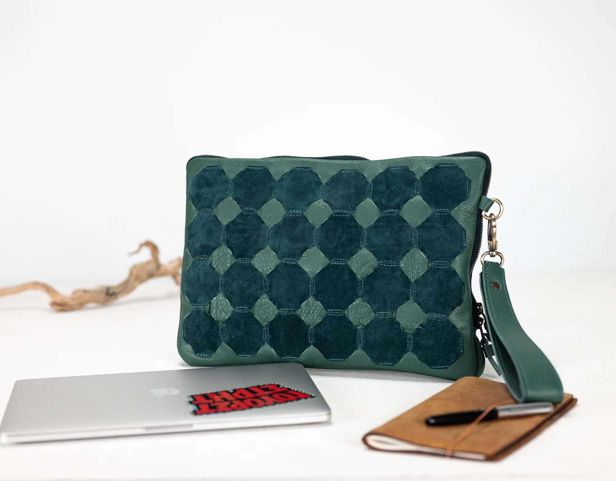 Green textured clutch bag on a white surface with a notebook and pen.