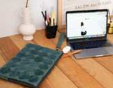 Laptop on a wooden desk with a floral laptop sleeve and office supplies.