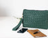 Green woven clutch bag with phone and notebook on a white background
