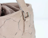 Close-up of a beige handbag with decorative stitching on a light background