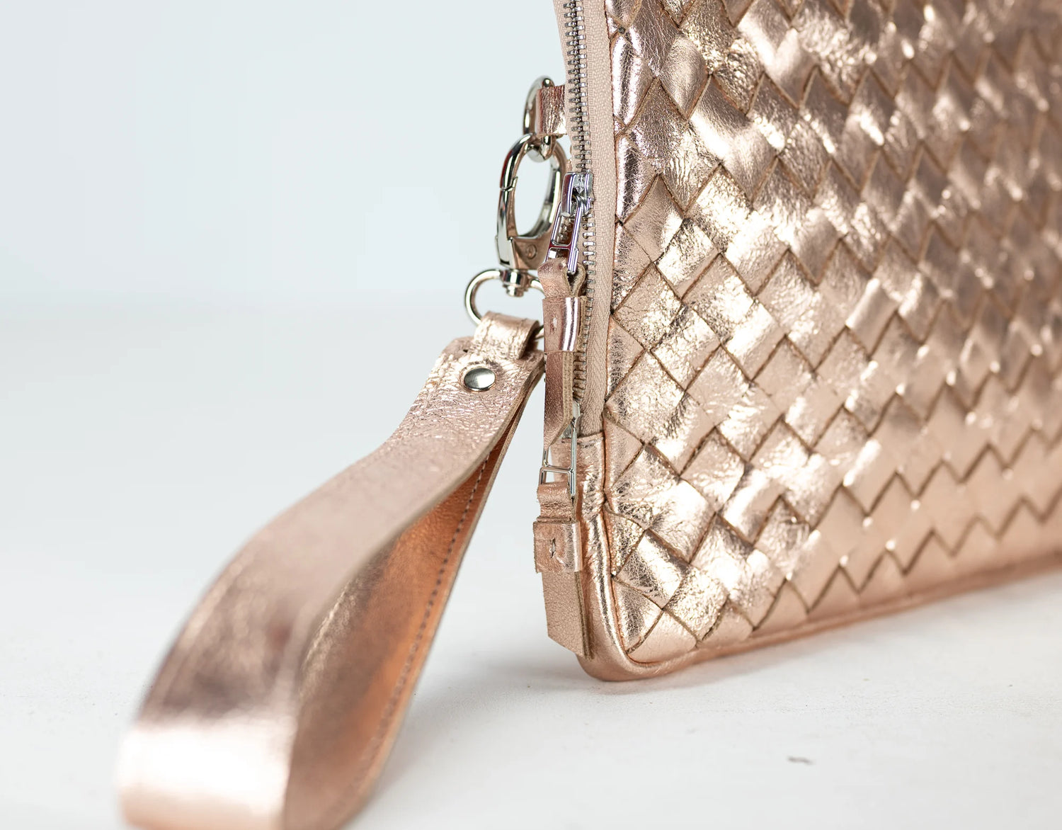 Rose gold clutch bag with woven pattern on a light gray background