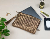 Woven brown leather pouch on a white surface with a laptop, keys, and other items.