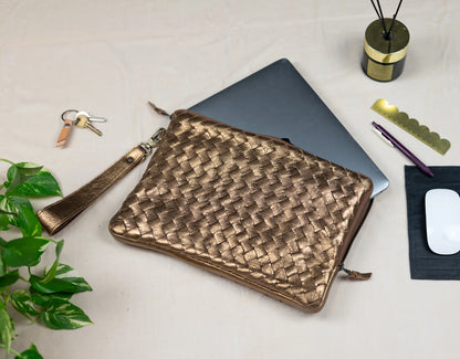Woven brown leather pouch on a white surface with a laptop, keys, and other items.
