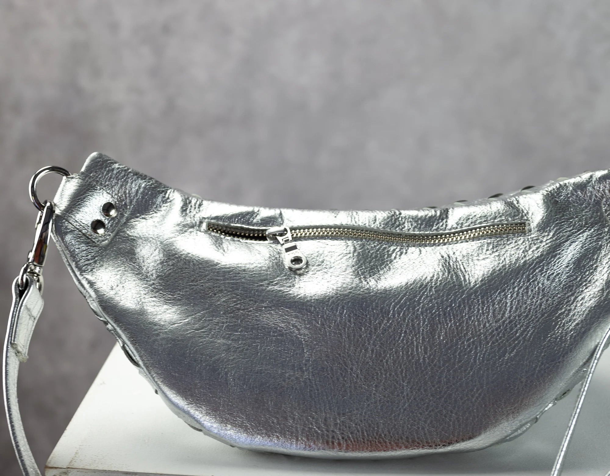 Silver leather handbag with a strap on a gray background
