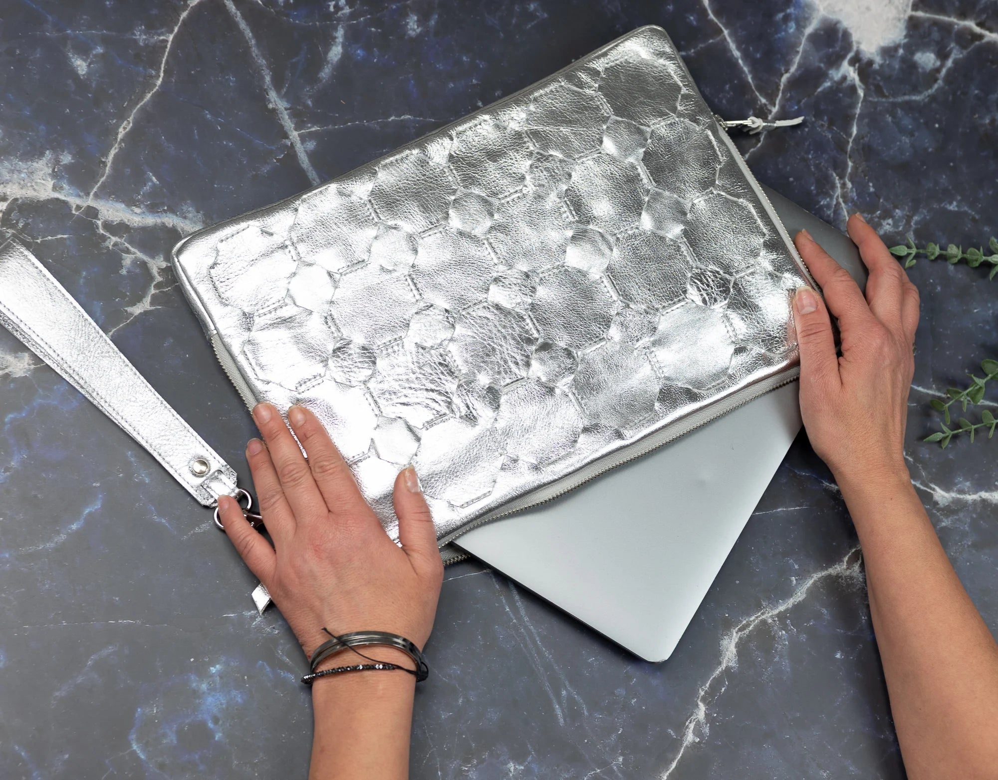 Person holding a silver metallic notebook on a dark marble surface