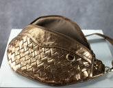 Gold woven handbag on a white surface with a gray background