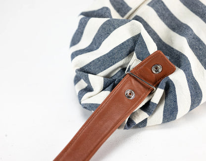 Blue and white striped bag with a brown leather strap on a light gray background