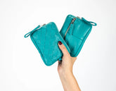 Turquoise leather clutch held by a hand on a white background