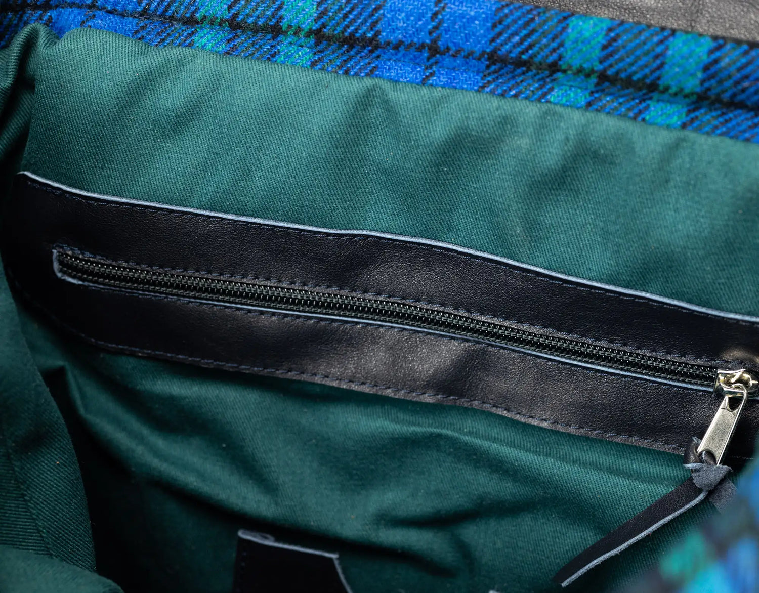 Close-up of a green fabric with a black zipper and plaid pattern in the background