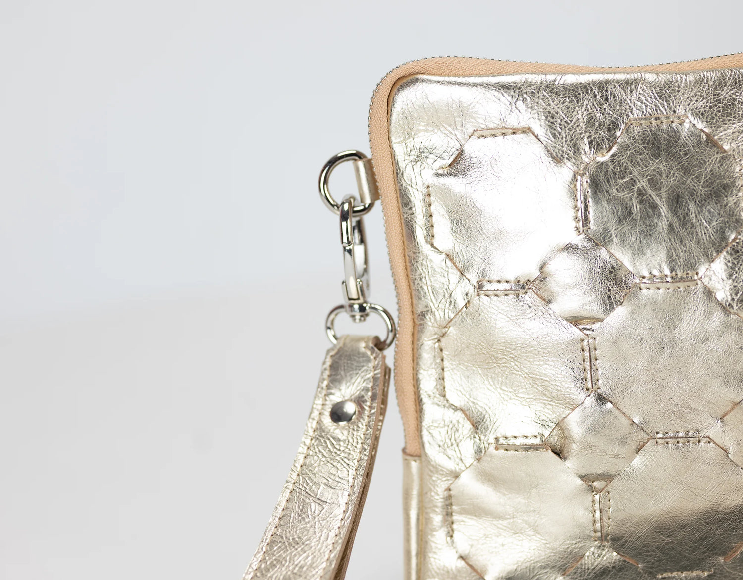 Metallic gold handbag with a strap on a light gray background