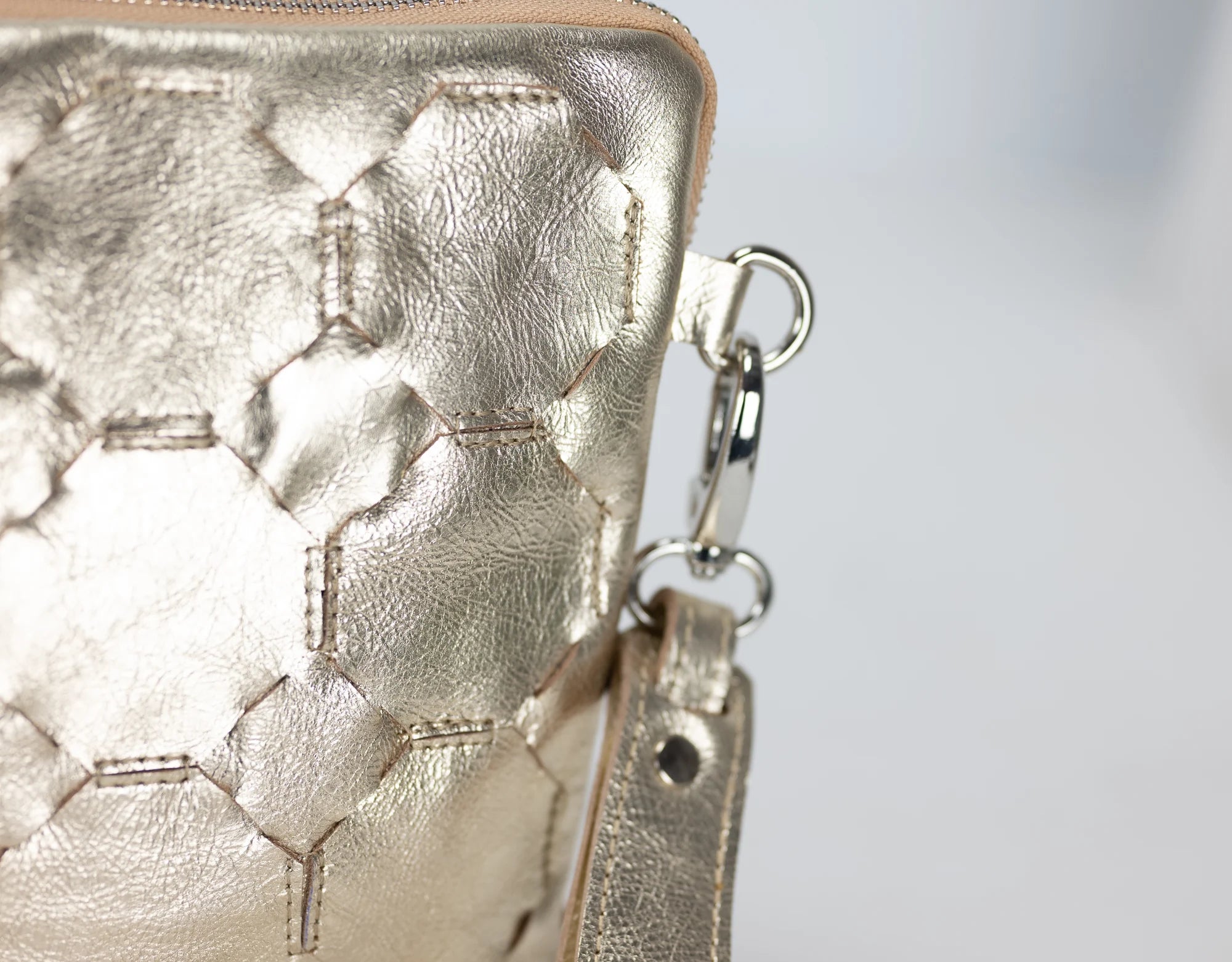 Close-up of a gold textured handbag with a keychain on a light gray background