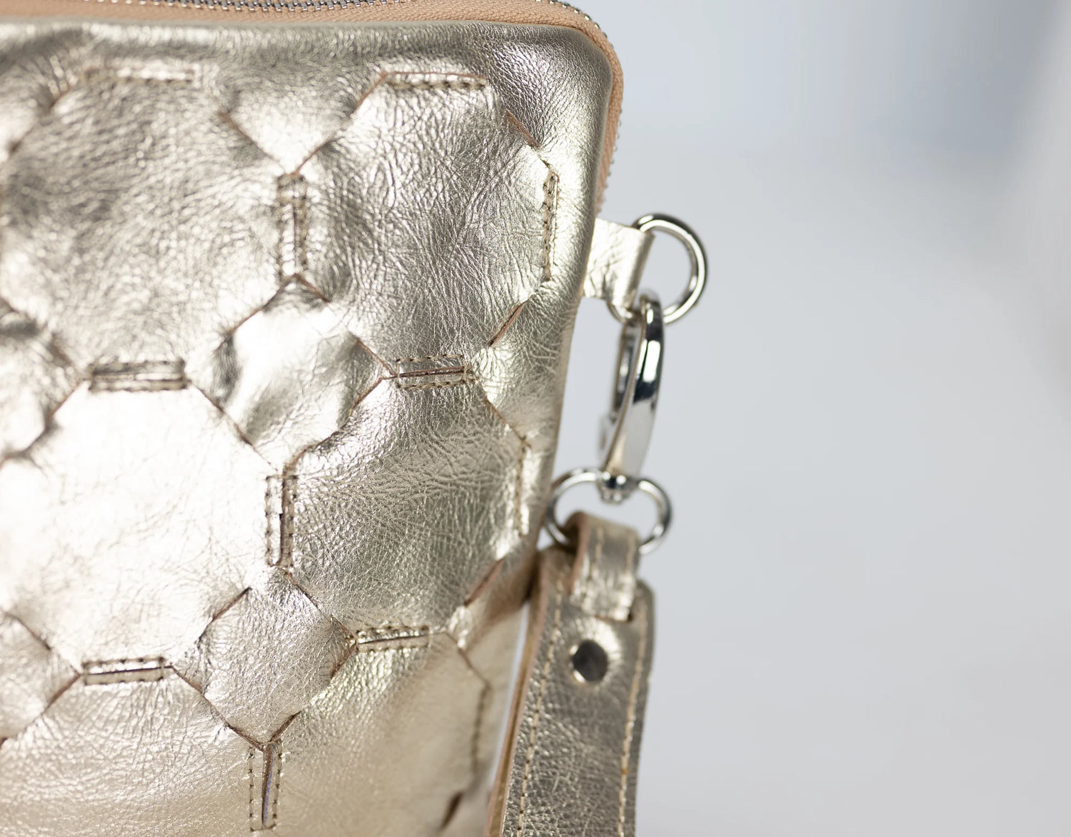 Close-up of a gold textured handbag with a chain detail on a light gray background