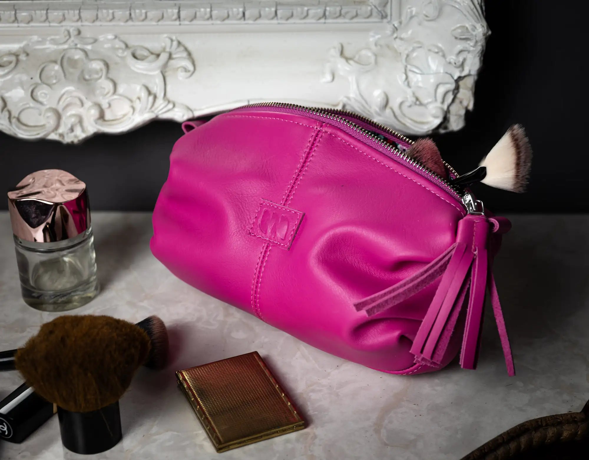 Pink makeup bag with cosmetic items on a decorative surface