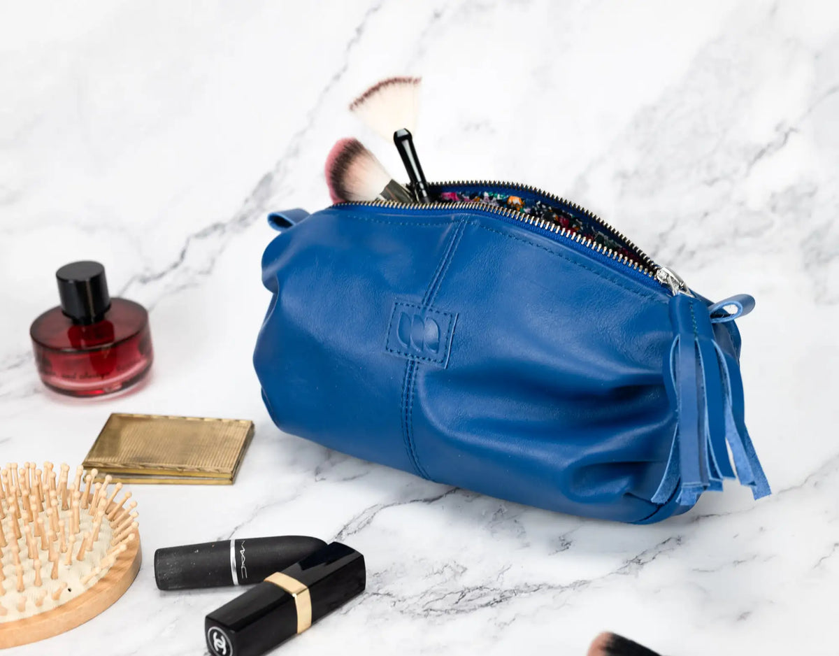 Blue makeup bag with cosmetic items on a marble surface#color_royal-blue