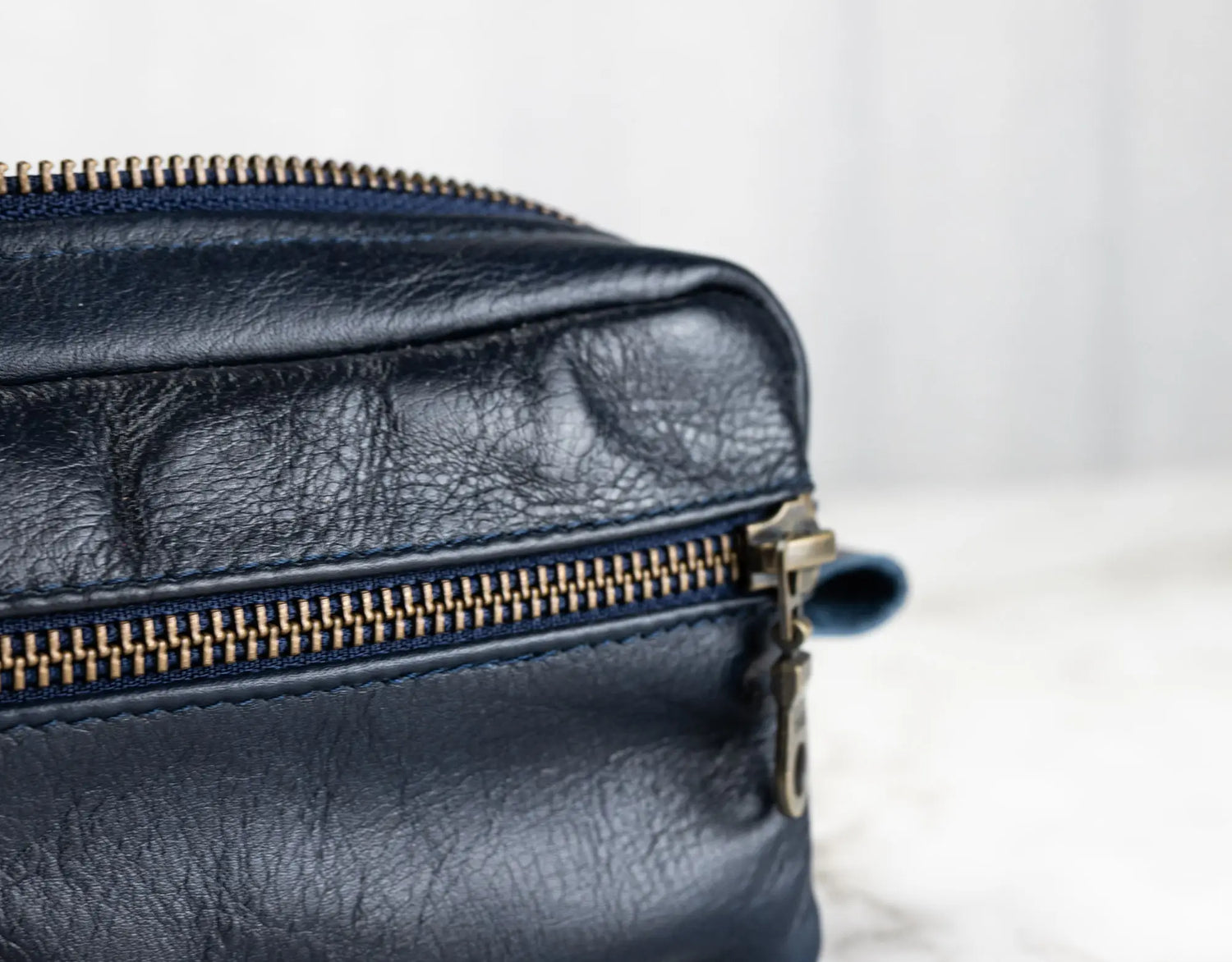 Close-up of a navy blue leather bag with a gold zipper on a light background