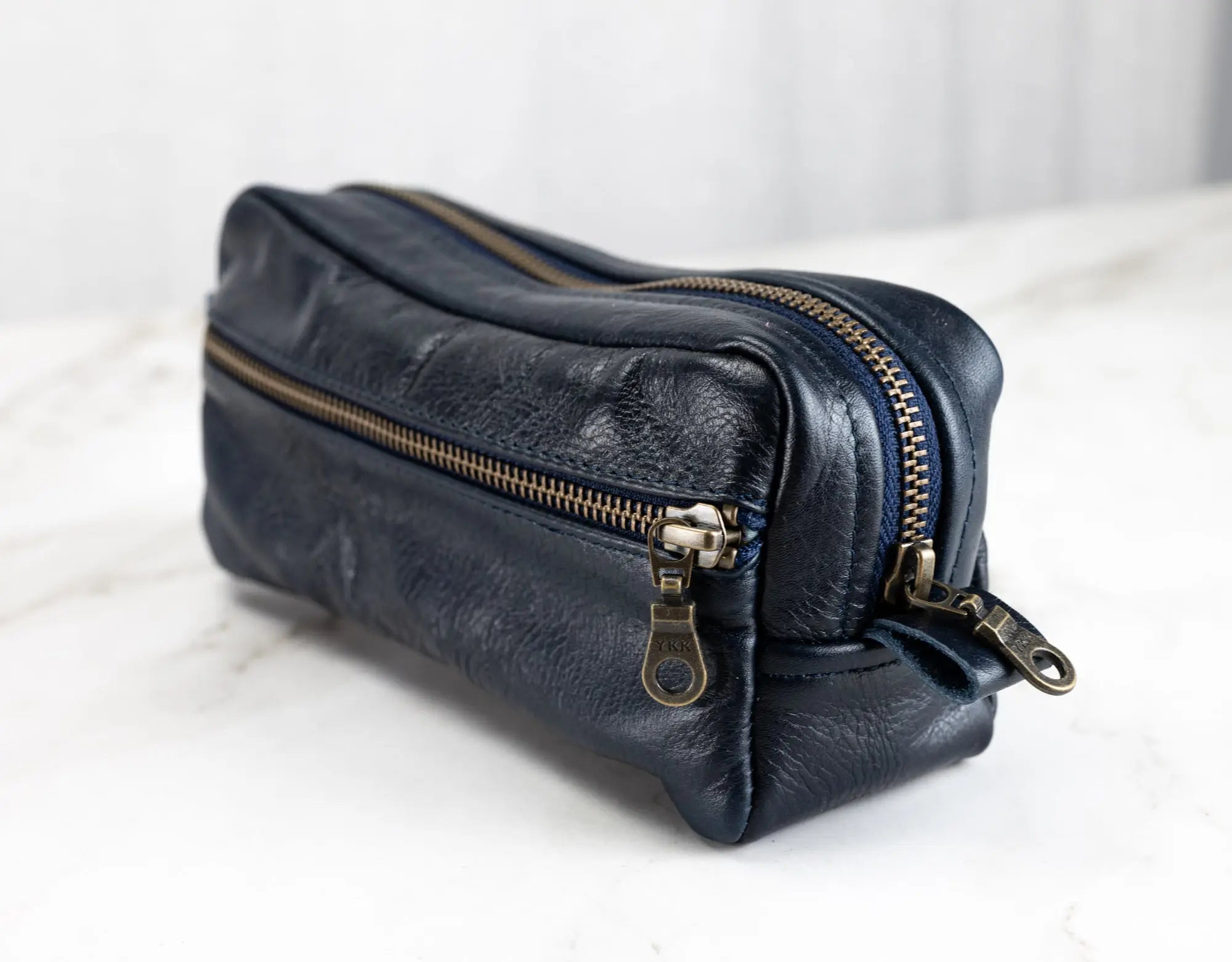 Blue leather pouch with gold zippers on a white surface
