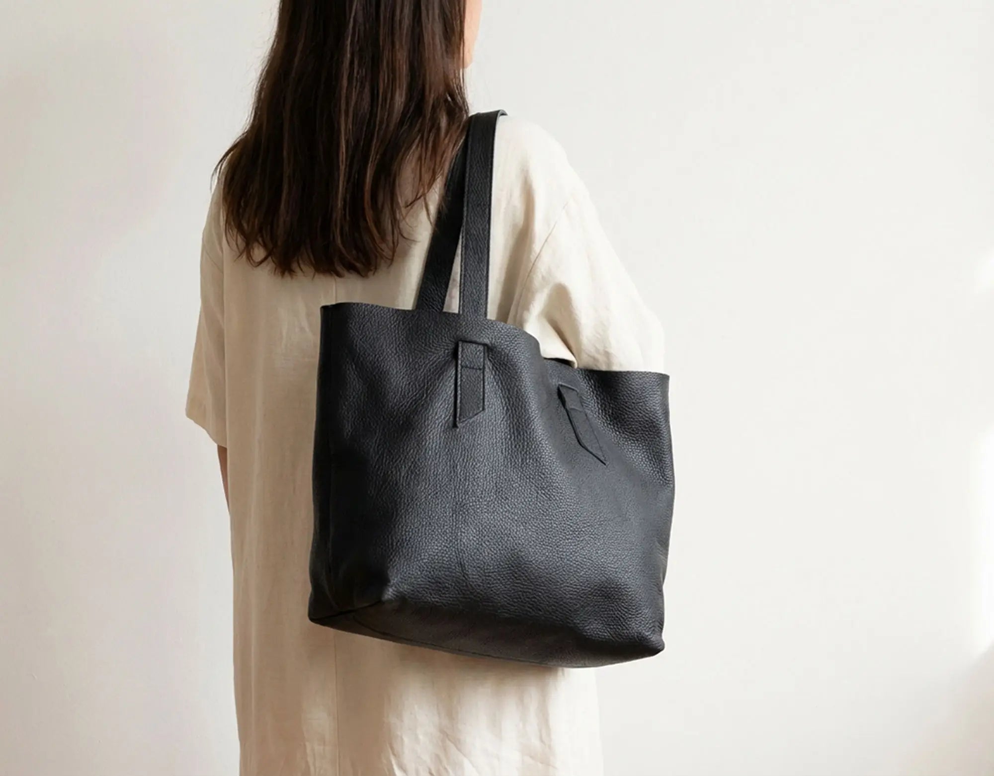 Person holding a black tote bag against a plain background