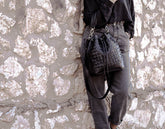 Person holding a textured black handbag against a stone wall