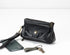 Black leather clutch with wrist strap, phone, and keys on a white background