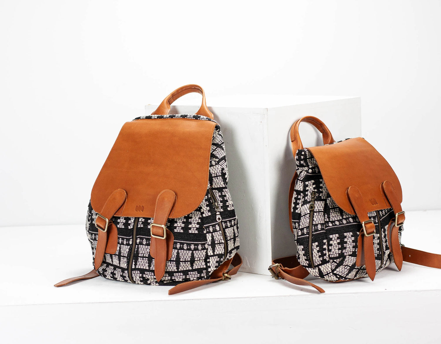 Two backpacks with patterned fabric and brown leather straps on a white background