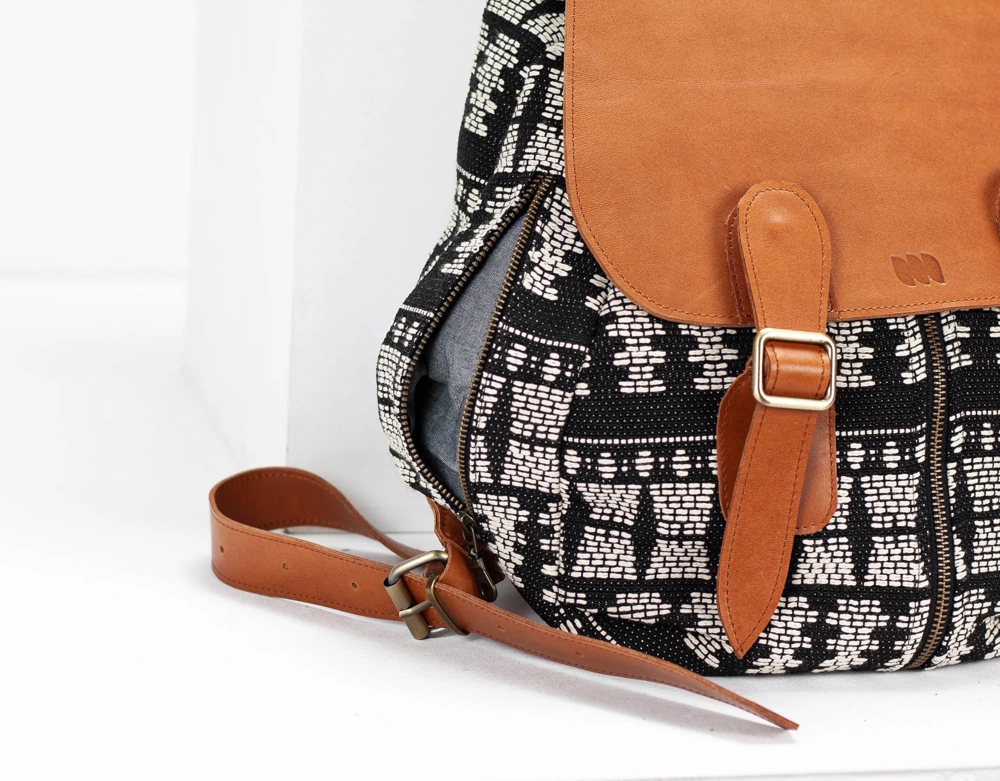 Black and white patterned bag with brown leather straps on a white background