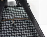 Close-up of a black and gray houndstooth patterned bag with a gold zipper on a white background.