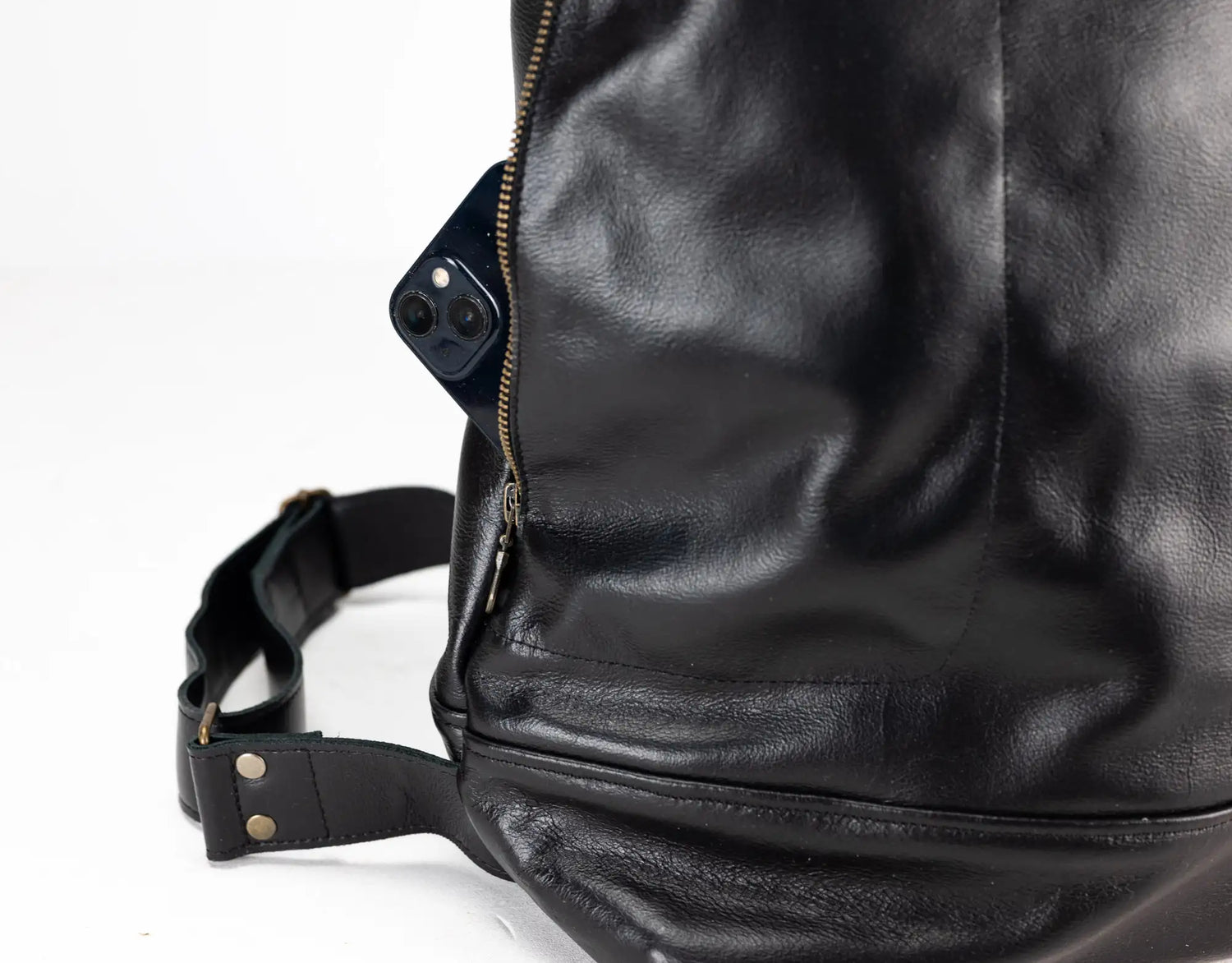 Close-up of a black leather bag with a strap on a white background