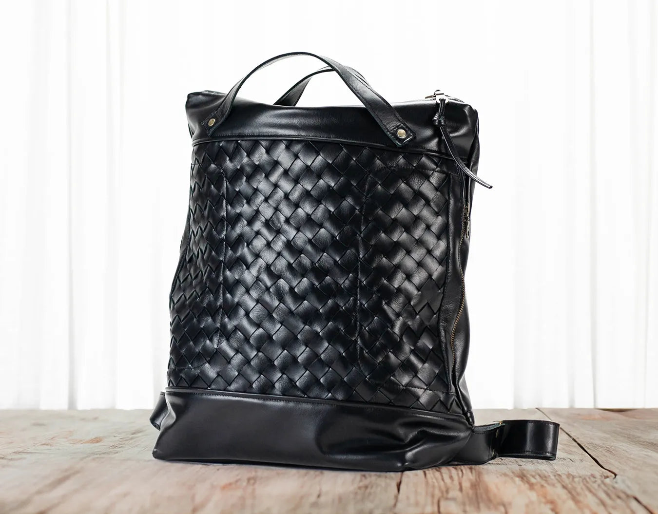 Black woven leather bag on a wooden surface with a white background