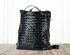Black woven leather bag on a wooden surface with a white background