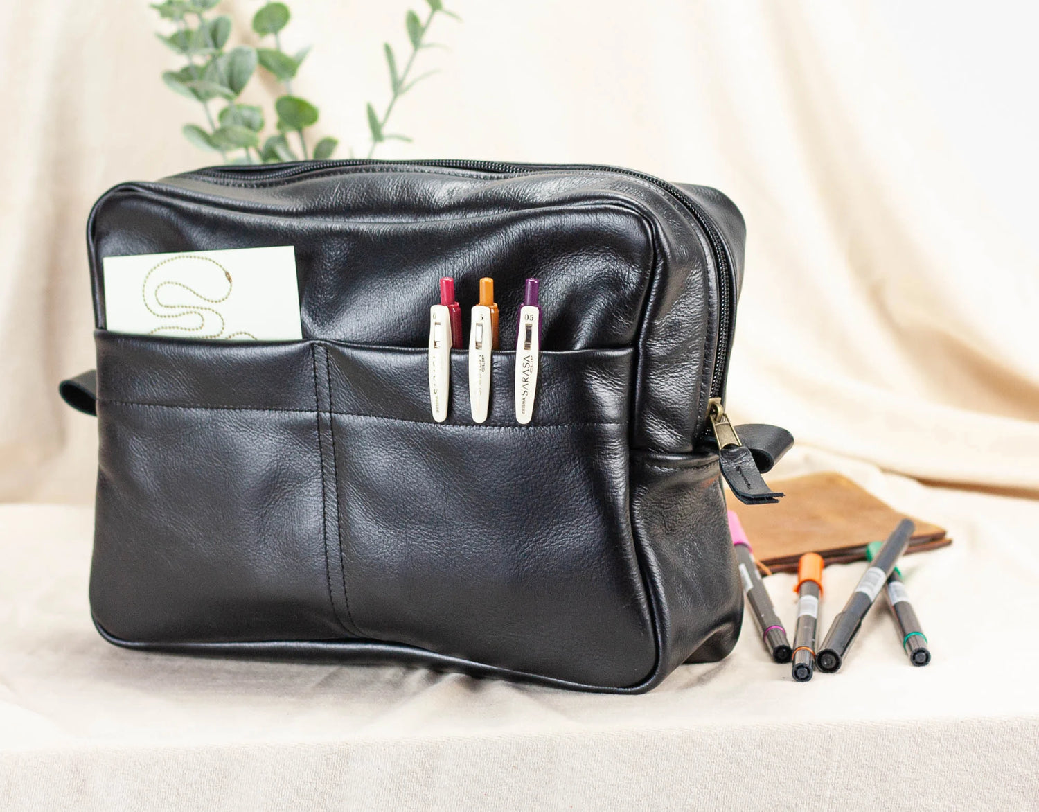 Black leather bag insert with pen holders and markers on a light background