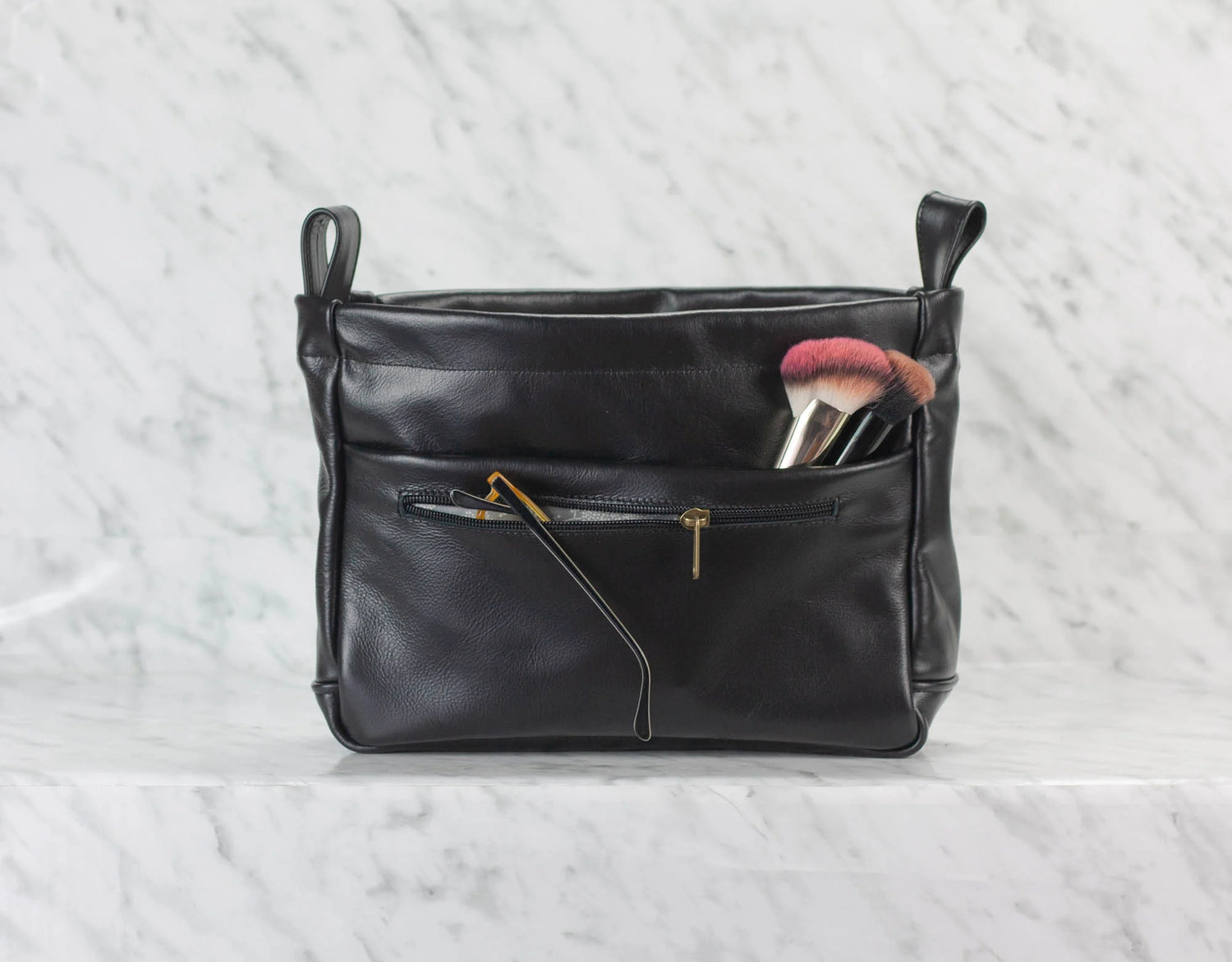 Black leather handbag with makeup brushes on a light gray background