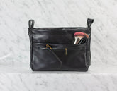 Black leather handbag with makeup brushes on a light gray background