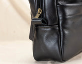 Close-up of a black leather bag with a gold zipper on a beige background
