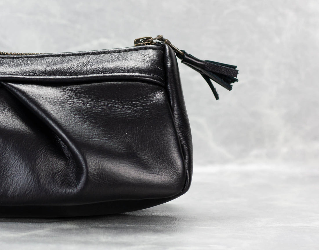 Black leather clutch bag with a tassel on a light gray background