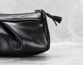 Black leather clutch bag with a tassel on a light gray background