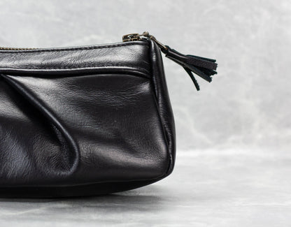 Black leather clutch bag with a tassel on a light gray background