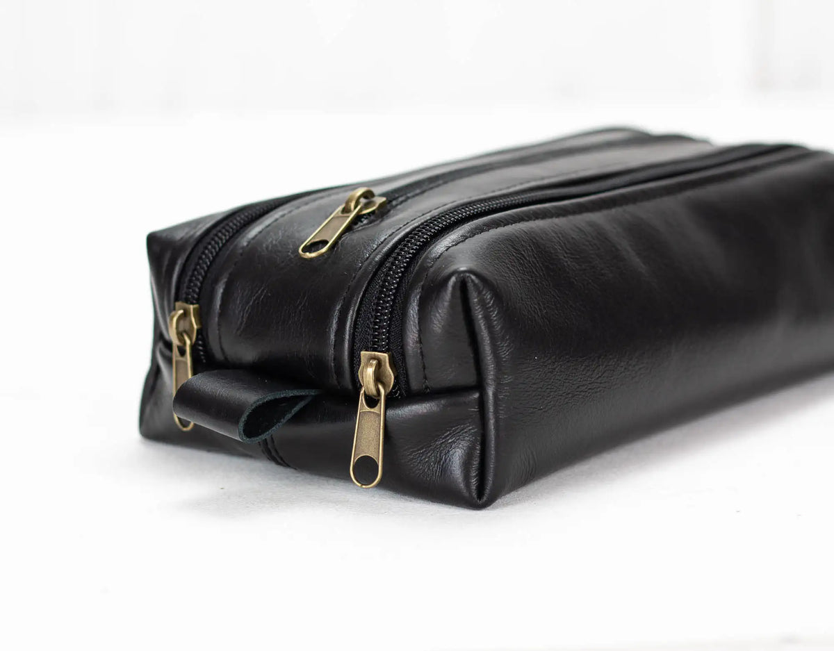Black leather toiletry bag with brass  zippers on a white background#color_black