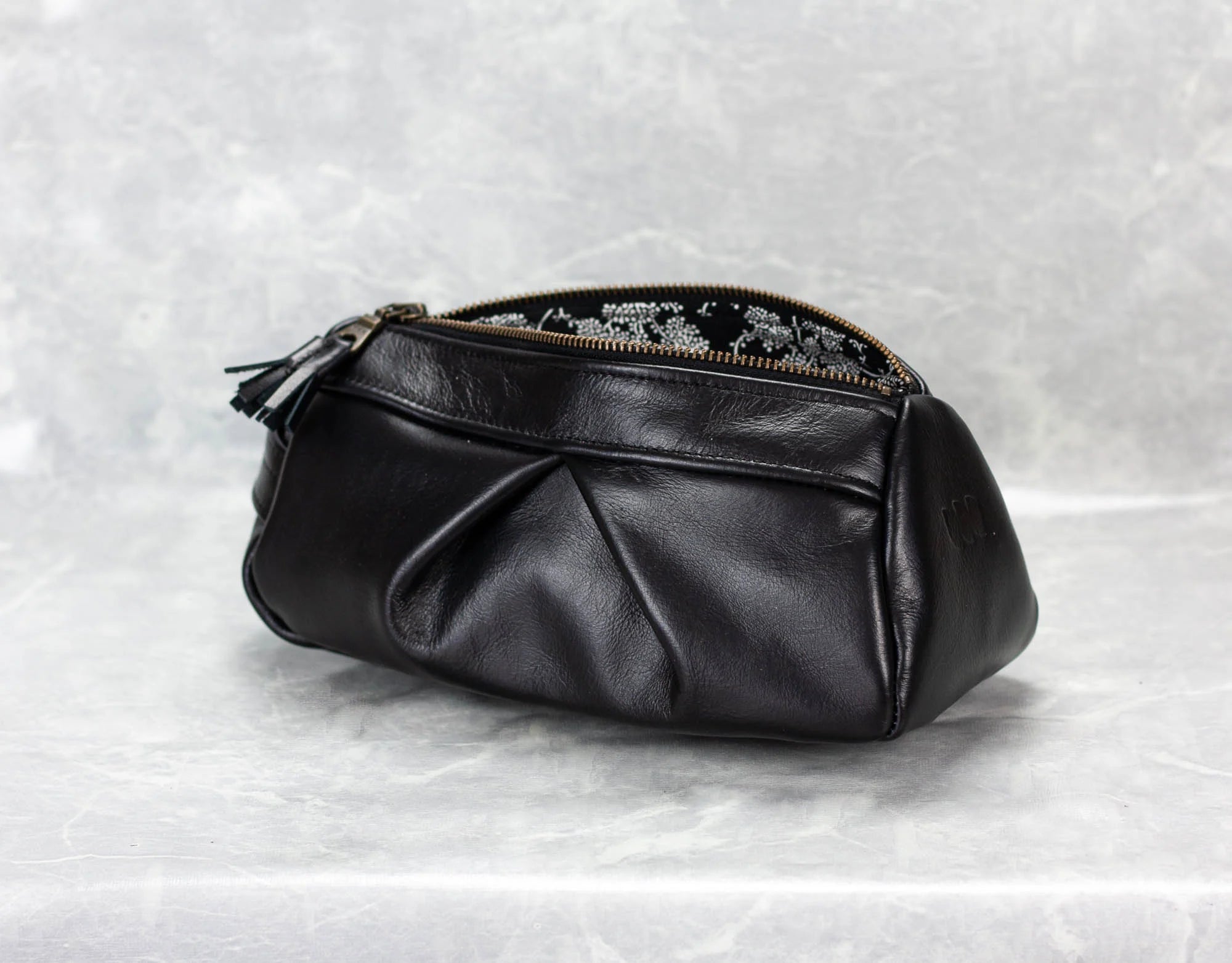 Black leather pouch with floral embroidery on a textured white background