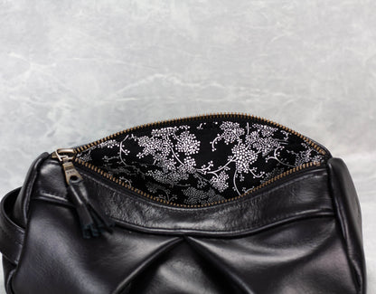 Black leather bag with floral embroidery on a textured gray background