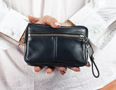 Person holding a black leather wallet with a strap on a white background
