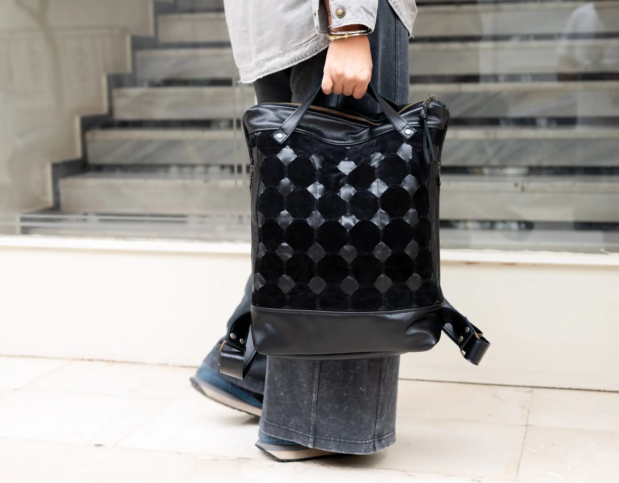 Person holding a black textured backpack on a light-colored floor.