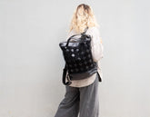 Person wearing a black backpack with a pattern against a plain background