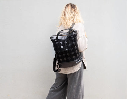 Person wearing a black backpack with a pattern against a plain background