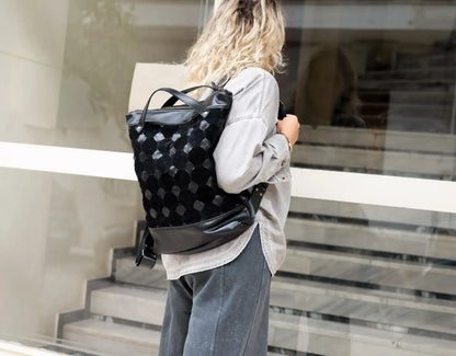 Person carrying a black patterned backpack outside a building