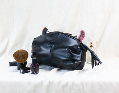 Black leather pouch with makeup items on a white background