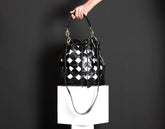Black and white checkered handbag held by a person against a dark background