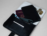 Black leather wallet with phone, cards, and coins on a light gray background