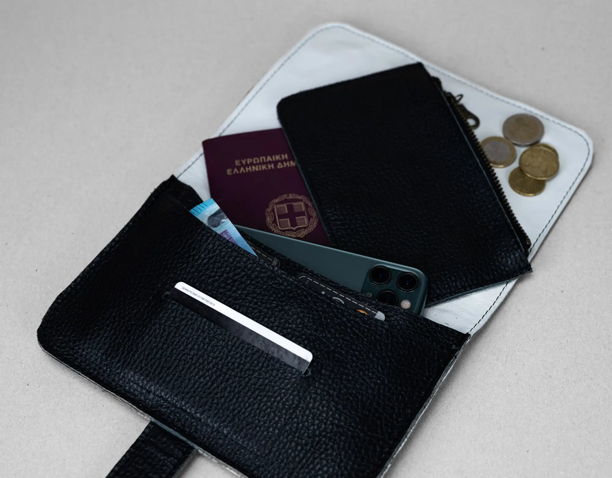 Black leather wallet with phone, cards, and coins on a light gray background
